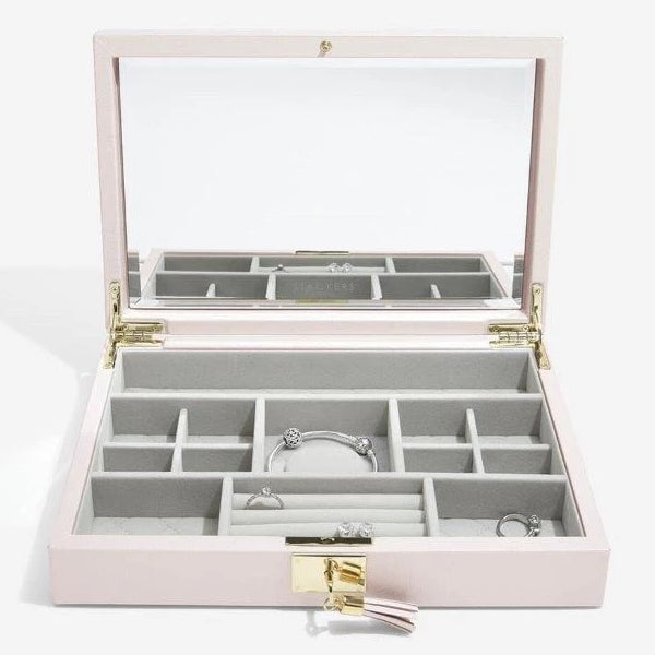 Stackers Leather Jewellery Box 75449 Blossom Pink Leather Lidded. This beautifully luxurious leather jewellery box is ideal for housing your jewellery collection, from necklaces and bracelets to rings and earrings. This lid includes a fitted ring roll and 12 storage sections, with a wide, primary section perfect for keeping necklaces tangle-free. Complete with an interior mirror and finished with gold detailing as well as a lock with leather tasseled key, to keep your sentimental items safe and secure.